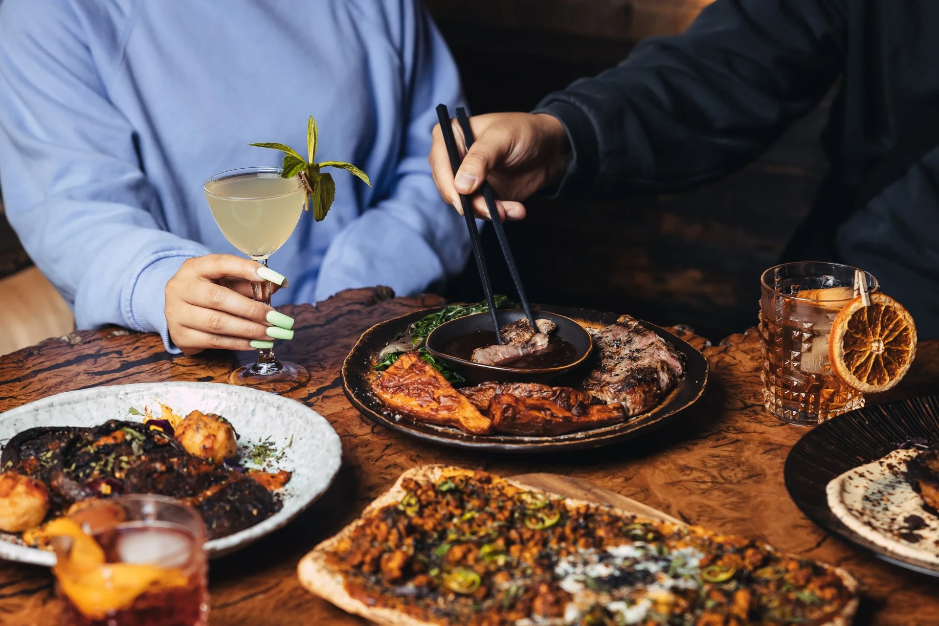 Guests sharing steak and cocktails at Saga Bar