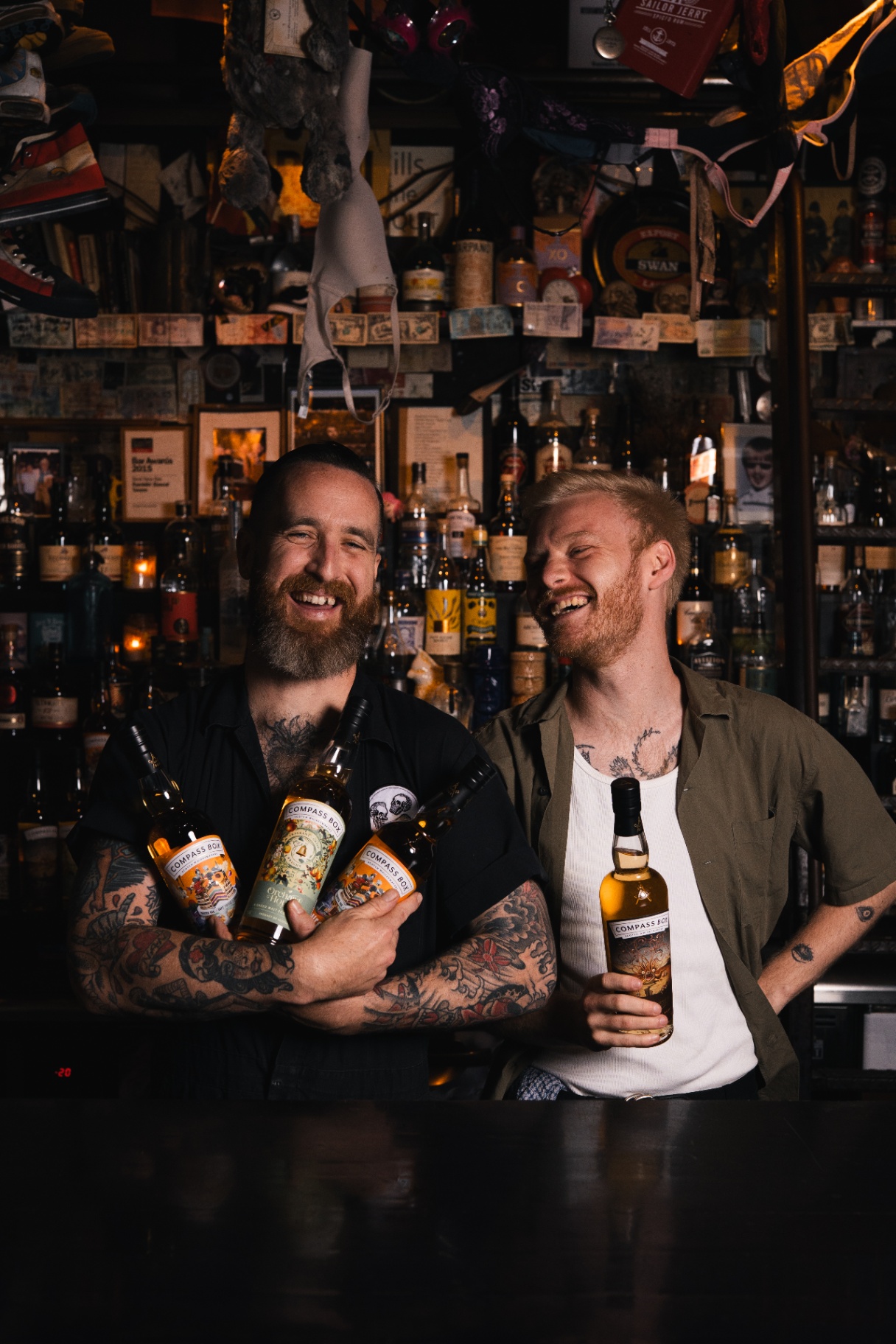 Two bartenders laughing with whisky bottles