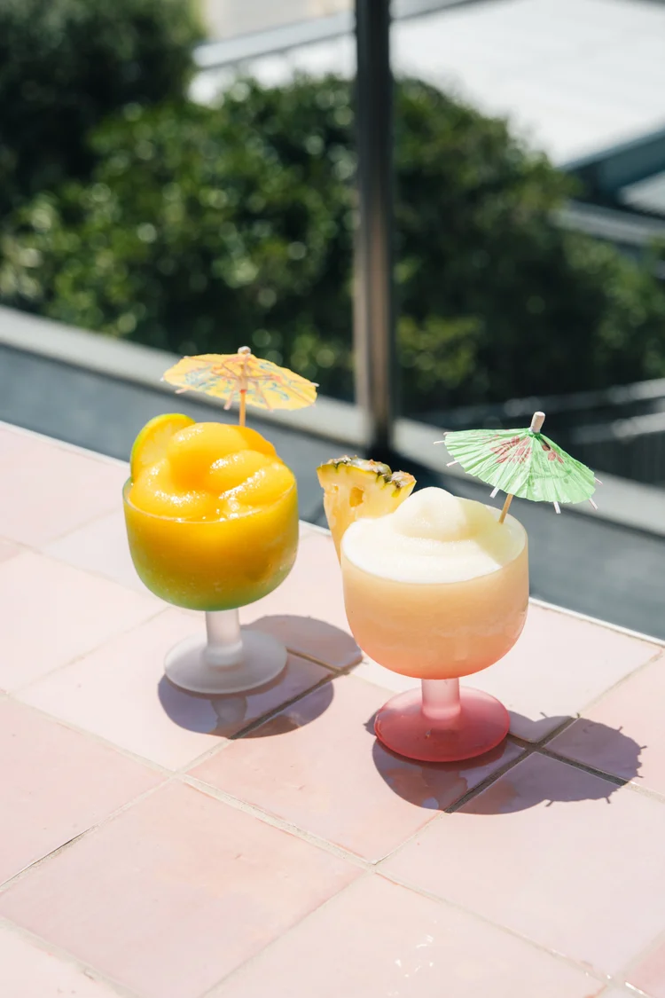Two frozen daiquiris with cocktail umbrellas on pink tiles