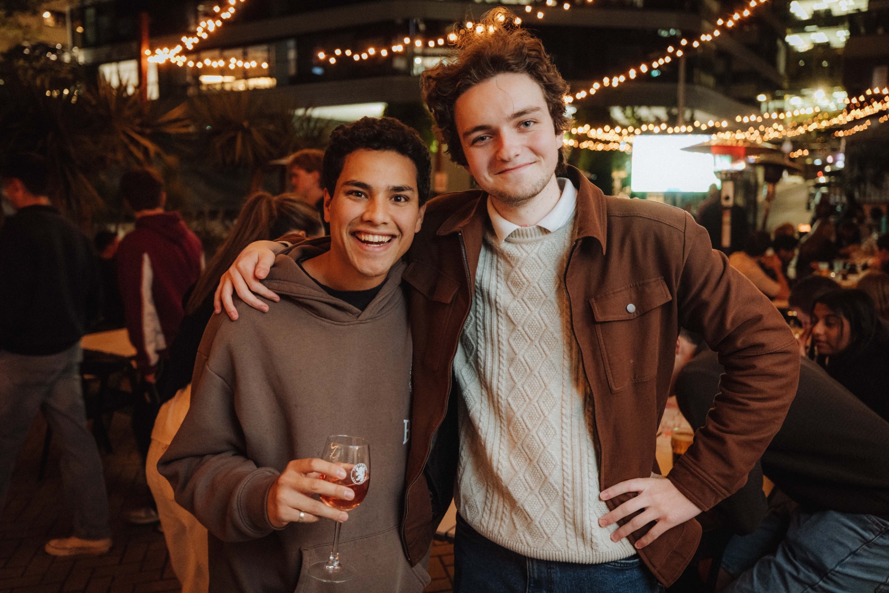 Two friends at an outdoor bar under fairy lights